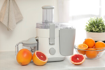 Modern juicer and grapefruits on white counter in kitchen