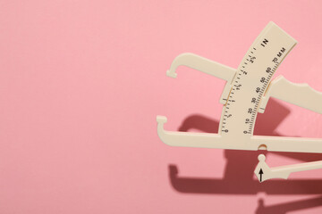 Plastic body fat caliper on pink background. Space for text