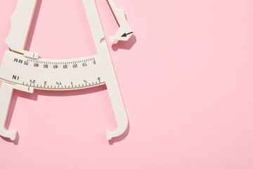 Plastic body fat caliper on pink background, top view. Space for text