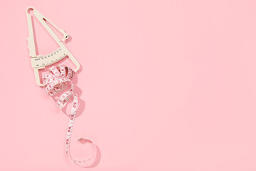 Body fat caliper and measuring tape on pink background, top view. Space for text