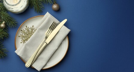 Beautiful Christmas setting with plate, elegant cutlery and festive decor on blue table, flat lay. Space for text