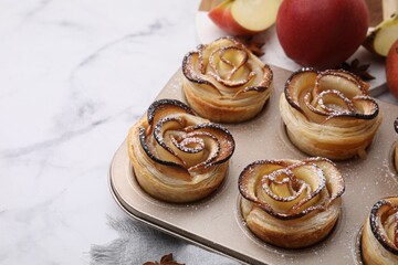 Freshly baked apple roses in cupcake pan on white marble table, closeup. Puff pastry