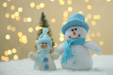 Cute decorative snowmen on artificial snow against blurred lights, closeup