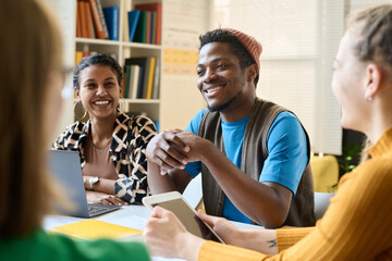Portrait of Black young student smiling while sitting at table and working together during class in school or college