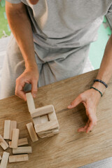 person stacks wooden blocks to construct tower on table in a room, Man playing table game for concentration at home. Digital detox
