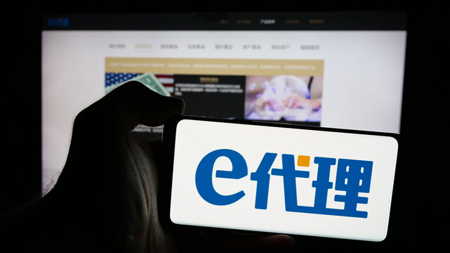Stuttgart, Germany - 08-28-2024: Person holding mobile phone with logo of Chinese financial platform company eDaili in front of business web page. Focus on phone display.