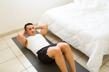 Fit hispanic man is working his abs while doing crunches on a yoga mat in his bedroom