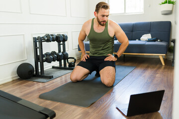 Healthy man pausing to catch his breath during an online home workout session on his laptop