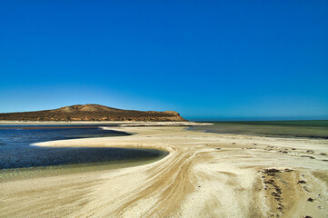 Sandbar at low tide in the transparent shallow tropical waters of Shark Bay, Whale Bone Point, Denham, Western Australia. In the background the coast of Peron Peninsula.
