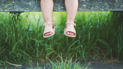 Toddler feet relaxing on a bench with the grass in background