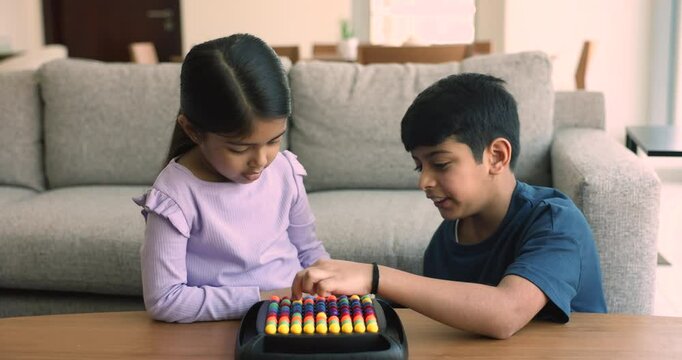 Focused engaged Indian sibling kids playing learning board game at home, moving colorful balls in board, solving puzzle, talking. Little sister girl teaching elder preteen brother boy to play