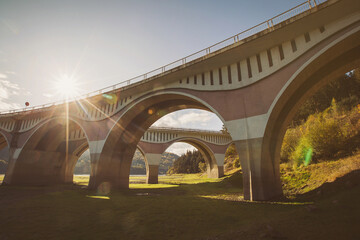 Fototapeta premium Viaduct in countryside of Romania. Old concrete bridge. View at viaduct and river on a mountain valley with Piatra Teiului lime stone, Bicaz Lake in Romania