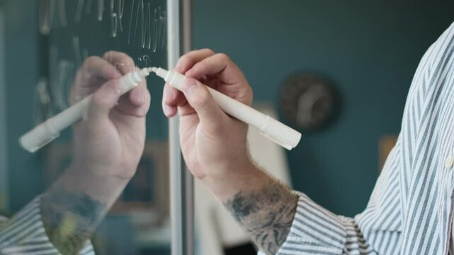 Hand of unrecognizable male programmer holding white pen writing code on glass wall in office