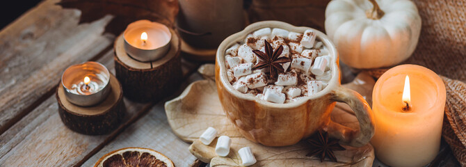 Spicy sweet fall hot drink: delicious pumpkin latte with cinnamon, marshmallow with salted caramel. Served in handmade artisan mug in shape of pumpkins, cozy home decor with candles, dry autumn leaves