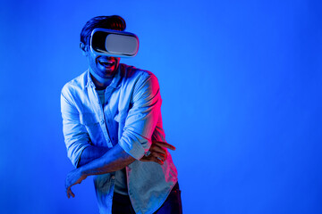 Handsome smart man dancing and moving gesture to music by using VR glasses with neon light background. Caucasian male gamer standing while moving to pop music wearing technology innovation. Deviation.