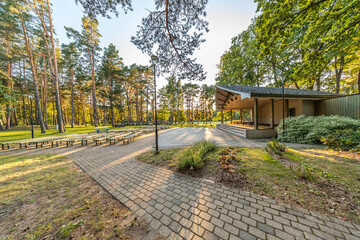 Fototapeta premium An outdoor amphitheater in a wooded park with long benches arranged in rows facing a stage, all under a canopy of tall trees.