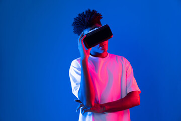 Surprised young African American looking through VR holding interesting object hologram on pink...