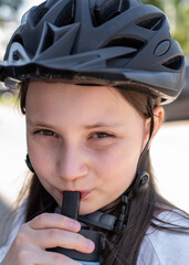 A 10-year-old girl in a bicycle helmet drinks water from a sports bottle.