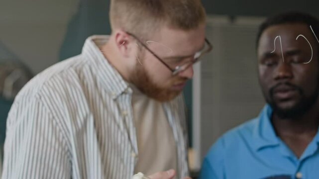 Young ethnically diverse programmers looking at digital tablet screen and writing code on glass wall in office