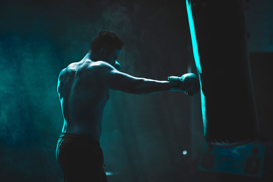 Man, punching bag and boxing exercise at gym, training practice and attack challenge for combat. Male person, neon and dojo club aesthetic for fight competition, athlete and martial arts workout