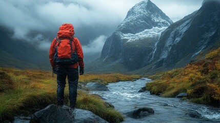 Person wearing a red jacket stands by a stream in a misty mountain landscape with rocky terrain and grassy patches