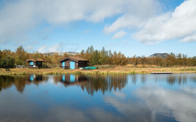Picturesque Norwegian fisherman's cabins known as "hytte" perched on shore overlook tranquil fjord calm waters with lush mountains forming serene idyllic Scandinavian landscape