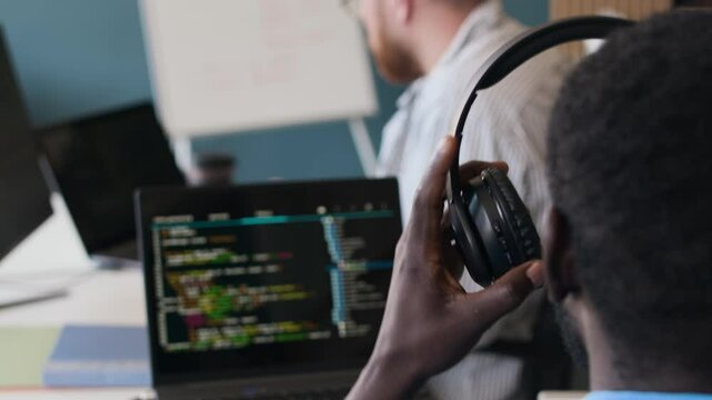 Rear view of unrecognizable African American programmer putting on headphones while working on code