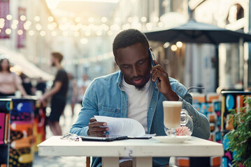 African american business man reads documents and speaking on smartphone sitting on outdoor cafe