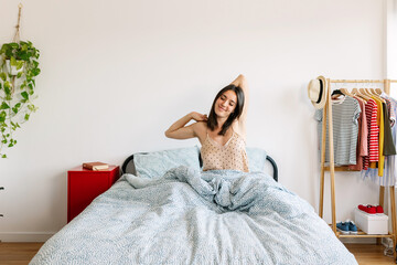 Happy woman waking up in the morning, stretching arms sitting on bed.