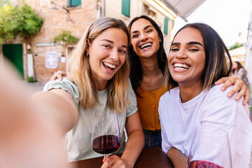Three happy young women enjoying summer vacation drinking red wine in a bar. Female friendship concept