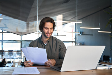 Happy busy young business man accountant reading file report documents checking data online looking...