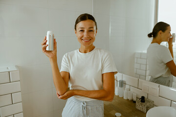A Joyful Smiling Woman Elegantly Showcasing a Skincare Product in a Modern Bathroom Setting