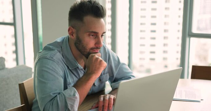 Pensive young Hispanic freelance professional man using laptop at workplace table, touching chin, thinking on creative ideas, typing, using desktop, computer for online work from home