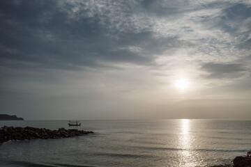 A serene scene of a traditional fishing boat gliding through calm waters during early morning hours in Prachuap Khiri Khan, Thailand. 