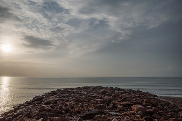 A peaceful seascape featuring a rocky shoreline under a soft, overcast sky during sunset. 