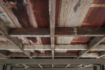 A close-up view of a rustic wooden ceiling featuring exposed wooden beams and aged wooden planks.