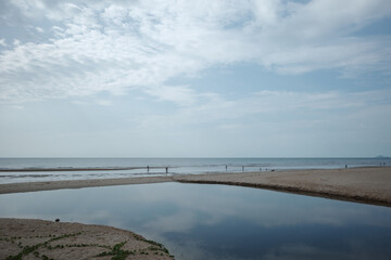 A serene coastal scene featuring a vast sandy beach under an expansive, cloudy blue sky.