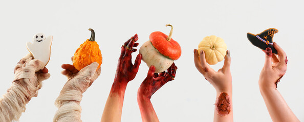 Zombie hands holding pumpkins and Halloween cookies on white background