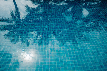 A serene and tranquil swimming pool with a mosaic tiled floor, capturing the reflection of palm trees and a bright sky. 