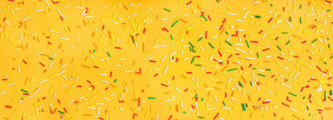 Sweet colorful sprinkles scattered on orange background
