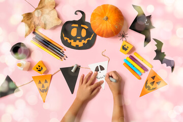 Hands of child making decorations for Halloween celebration on pink background
