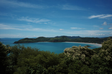 A stunning panoramic view of a tropical coastline featuring crystal-clear turquoise waters and green forested hills at Khao laem pu chao, Chon buri, Thailand. 