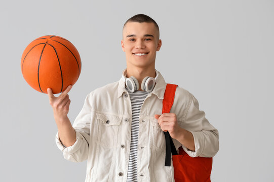 Male student with backpack, headphones and ball on grey background - Powered by Adobe