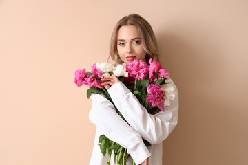 Young woman with beautiful peony flowers on beige background