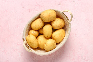 Wicker basket with raw baby potatoes on pink background