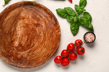 Wooden kitchen board, fresh tomatoes, sea salt and basil on light background