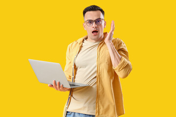 Stressed young man with laptop on yellow background. Deadline concept