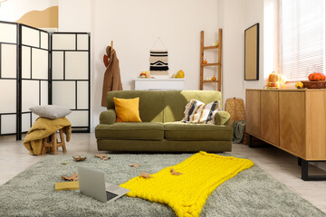 Naklejka premium Interior of living room with green sofa and fallen leaves