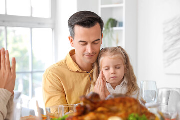 Little girl with her father praying before dinner at festive table on Thanksgiving Day