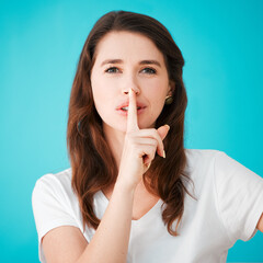 Naklejka premium Woman, portrait and silence in studio for secret, gossip and privacy for news. Person, finger on lips and attitude on blue background for shush, emoji gesture and sign for confidential storytelling